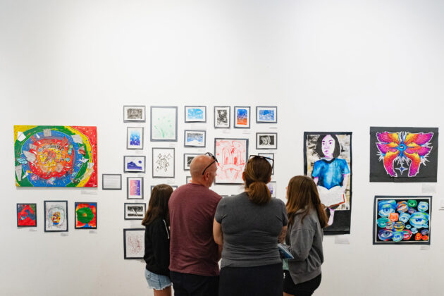 A group of four people from behind looking at art pieces on a wall.