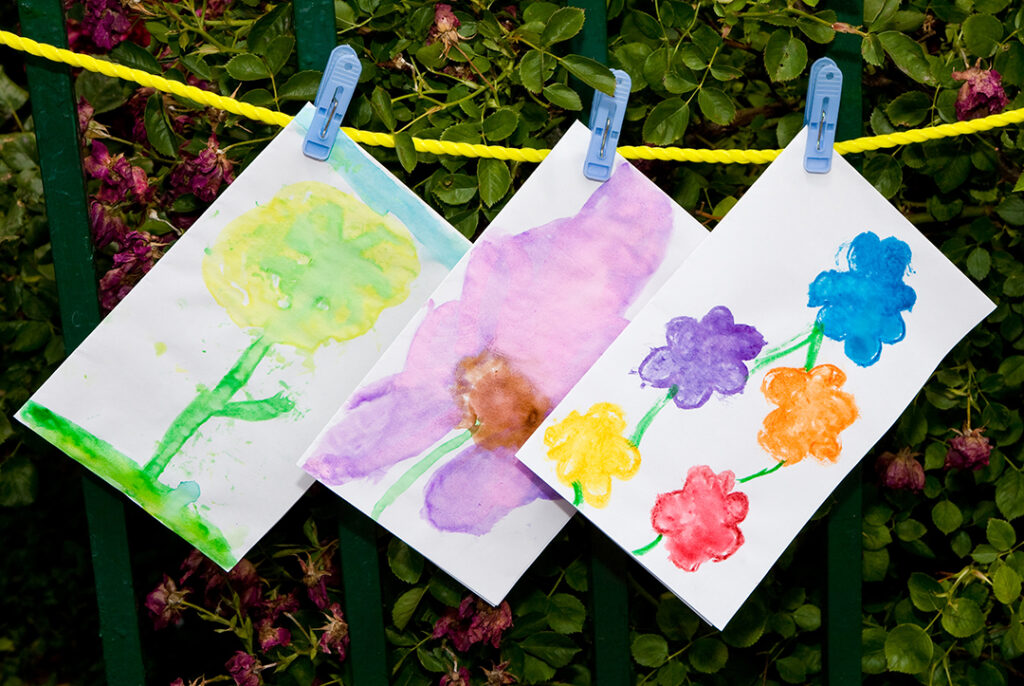Three paintings drying on a clothesline, most are of colorful flowers