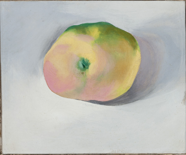 View from above of an apple on a light background. The apple is in shades of light peach, yellow and some green on the top.