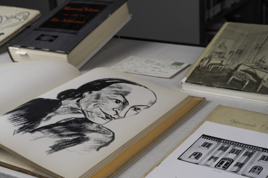 Close-up sketch of O'Keeffe in a cartoonish style in a display case with books and pamphlets.