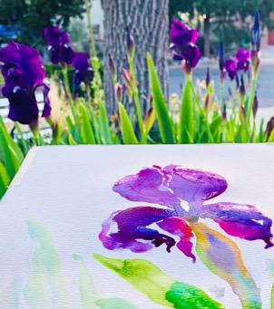 A watercolor painting of purple irises with real irises in the background.