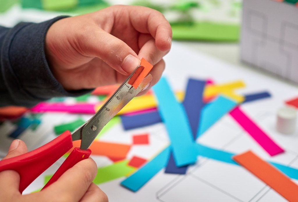 Close-up photograph of a child's hands as they cut small piece of colorful paper.