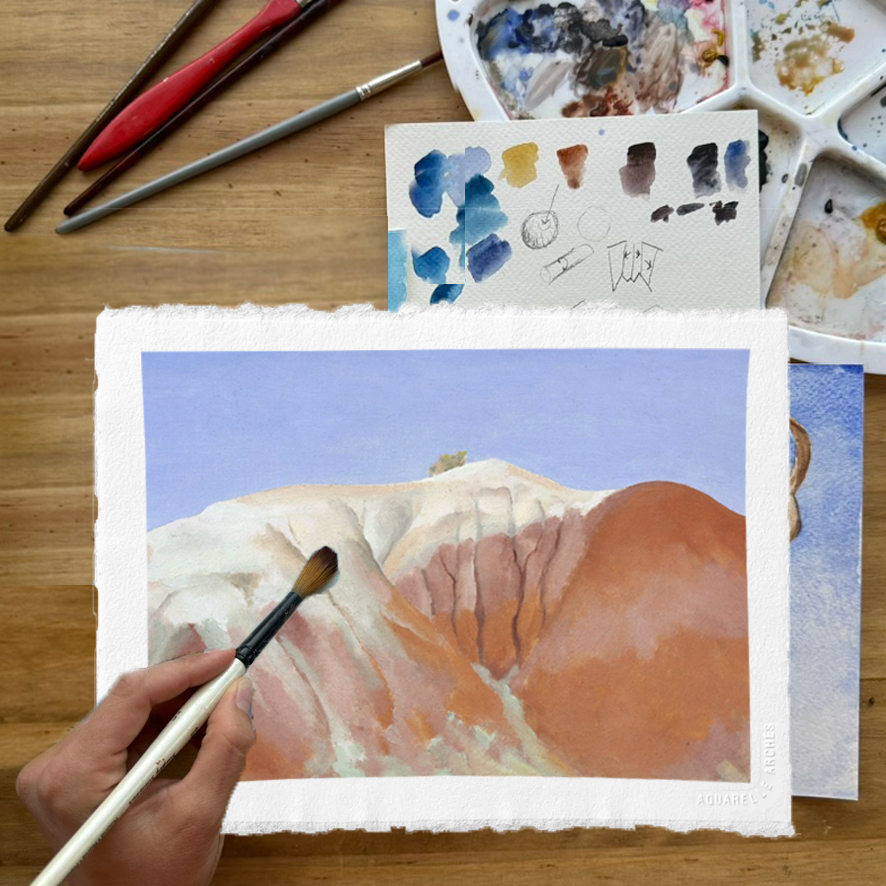 Photograph of a small canvas with a painting of a red and white hill with a blue sky. Above the canvas are a palette and brushes. On the bottom left of the frame, a hand holds a paint brush.