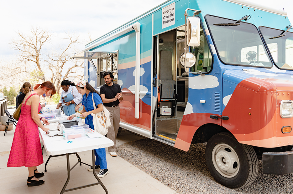 Photograph of the Art to G.O truck with tables and people engaging in art activities outside the truck.