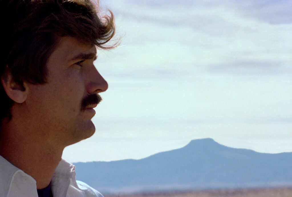 Juan Hamilton in profile taking up the left side of the frame. A blue flat-topped mountain and sky with clouds in the background.