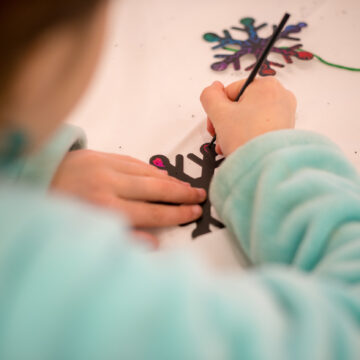 5. Closeup Photograph of a child painting wooden snowflake ornaments. The child is blurred and the camera is focused on their handiwork.