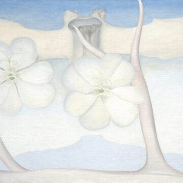 Large horizontal painting of blue and grey tones. Along the bottom in the foreground lies a bleached antler with arms reaching upward towards the sky. Floating along the top spanning the length of the canvas is a vertebral bone. Superimposed over this in the middle are two white flowers, hovering just above a blue silhouette of the Pedernal.