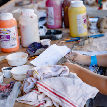 Close-up of a young person's hands as they mould clay on a table covered with paint and other art materials.