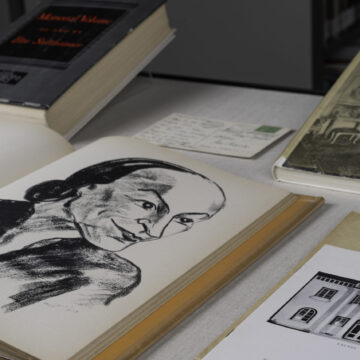 Close-up sketch of O'Keeffe in a cartoonish style in a display case with books and pamphlets.