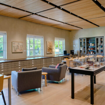 A view of the library and research center looking out the windows to the garden. There are three tables for research with seating and a bookcase.